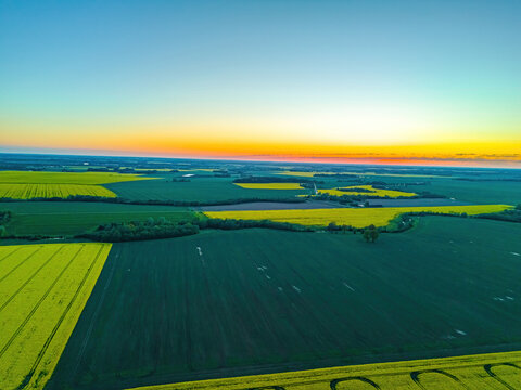 Aerial view of vibrant yellow rapeseed fields and green agricultural land under a colorful sunset sky in Jelgava, Latvia.