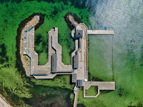 Aerial view of Skovshoved Havbad featuring its unique geometric wooden pier structure extending into clear turquoise waters, with people sunbathing on the decks in Gentofte, Denmark.