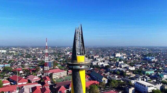 Aerial view of Monument of Pal 0 Banua tower rising above the urban cityscape with rooftops and a communication tower in Kecamatan Banjarmasin Tengah, Kalimantan Selatan, Indonesia.