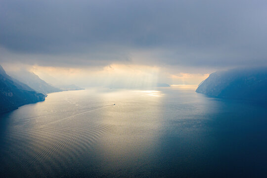 Aerial view of Lake Como with dramatic clouds and sun rays illuminating the water surface, surrounded by mountains in Lombardy, Italy.