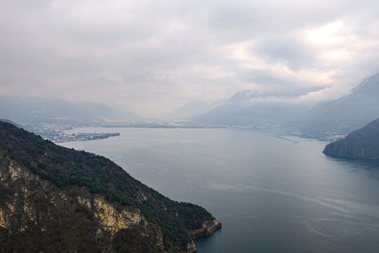 Aerial view of Lake Como surrounded by mountains and lush hills under a cloudy sky in Lombardy, Italy.