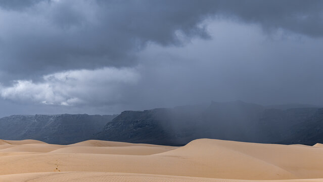 View of sand dunes under a dramatic stormy sky with dark clouds and distant mountains in Da'ira, Socotra, Yemen.