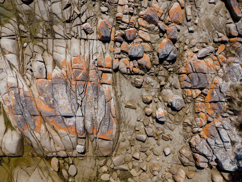 Aerial view of orange lichen-covered granite boulders along the rocky coastline of the St Helens Conservation Area in St Helens, Tasmania, Australia.