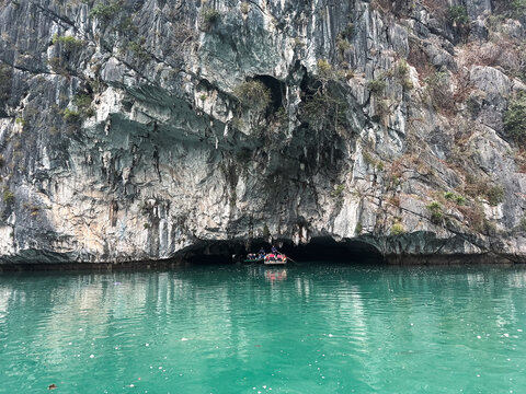 Vietnam - 05 February 2026: View of a small boat entering a limestone cave in Halong Bay with turquoise water and towering karst cliffs.