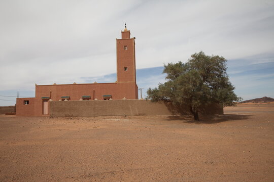 View of a traditional earthen mosque with a minaret standing in the arid desert landscape of Morocco.