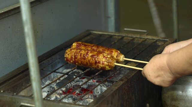 A scene of two ears of corn being grilled over charcoal at a stall in a Taiwanese night market.