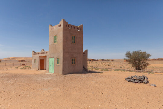 View of a traditional earthen adobe building standing in the arid desert landscape under a clear blue sky in Morocco.