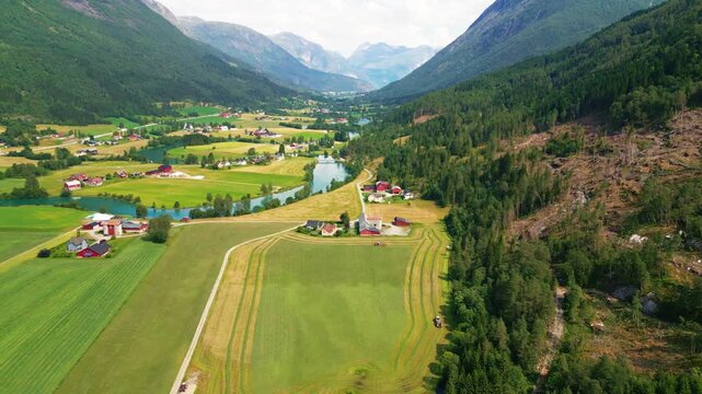 Aerial view of Stryn valley with a winding river, lush green fields, traditional red wooden houses, and surrounding mountains in Stryn, Vestland, Norway.
