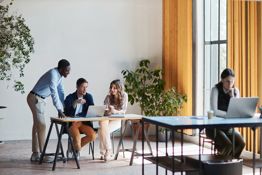 Diverse business team collaborating and discussing a project on a laptop in a modern co-working office, focusing on innovation, teamwork, and startup growth