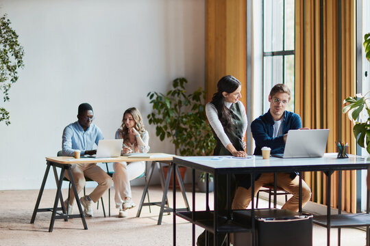Diverse team collaborating on business strategy in a modern coworking space, young professionals networking, discussing ideas, and working on laptops at shared desks