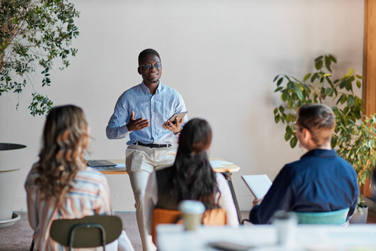 African american business professional delivering a presentation, leading a diverse team meeting, sharing ideas, and providing training during an office conference