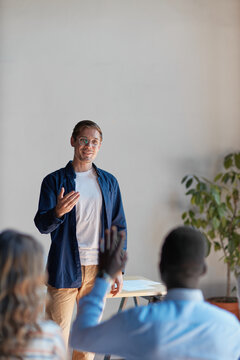 Speaker engaging audience in an educational workshop, presenting information and encouraging participation during a business seminar, answering a question from a raising hand