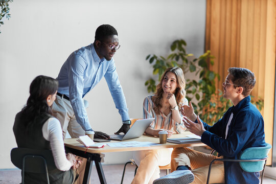 Group of diverse business people actively collaborating and communicating around a table in a modern office, sharing ideas and working together on a project