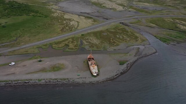 Aerial view of the rusted Gardar BA 64 shipwreck resting on a gravel beach near the dark waters of the coast in Saudlauksdalur, Vesturbyggd, Iceland.