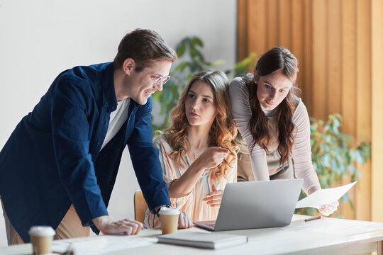 Diverse business team collaborating and brainstorming, discussing strategy and reviewing data on a laptop, fostering innovation in a modern office