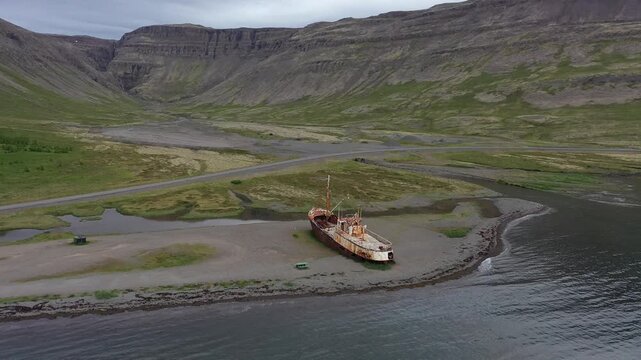 Aerial view of the historic Gardar BA 64 shipwreck resting on the shore with rugged mountains and green landscape in SAUDLAUKSDALUR, VESTURBYGGD, ICELAND.