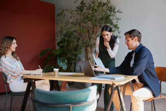Business colleagues collaborating at a meeting, analyzing data on a laptop and reviewing documents, discussing a new project while working together in a modern office