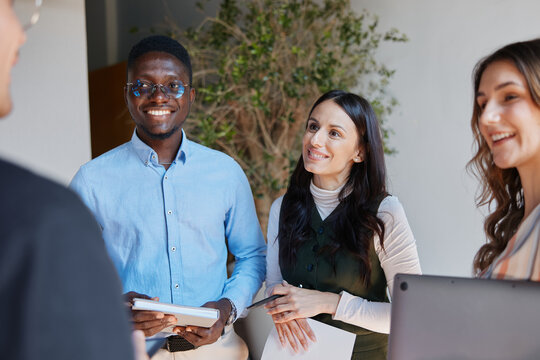 Diverse business professionals smiling, collaborating, and engaging in conversation during a team meeting in a modern office, showing teamwork and unity