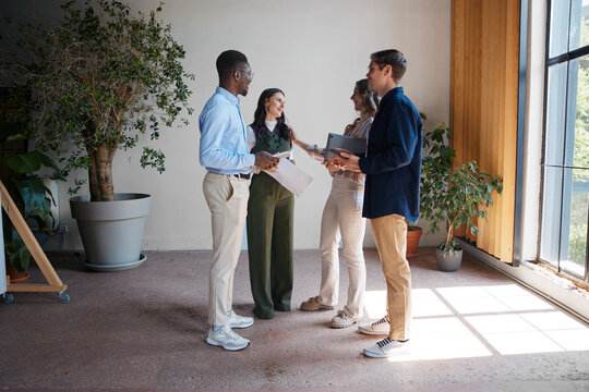 Diverse business professionals having informal meeting in modern office space, collaborating on project, sharing ideas, and discussing work in a corporate environment