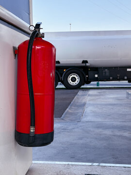 Red fire extinguisher at fuel station with tanker truck.