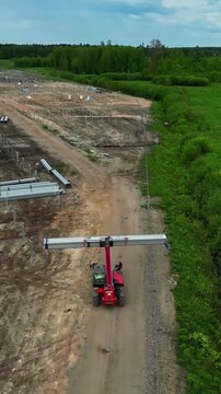 Aerial view of a red telehandler carrying metal beams on a dirt road at a construction site in Latvia.