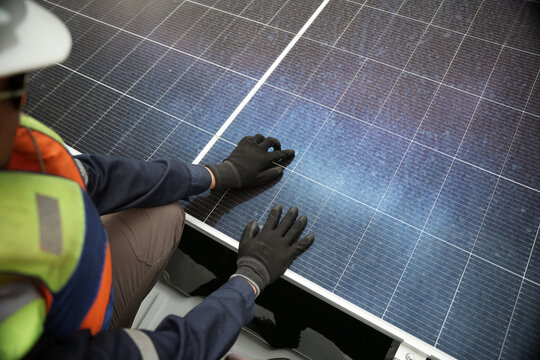 Aerial view of a technician in a high-visibility vest and gloves inspecting a solar panel in Berau Regency, East Kalimantan, Indonesia.