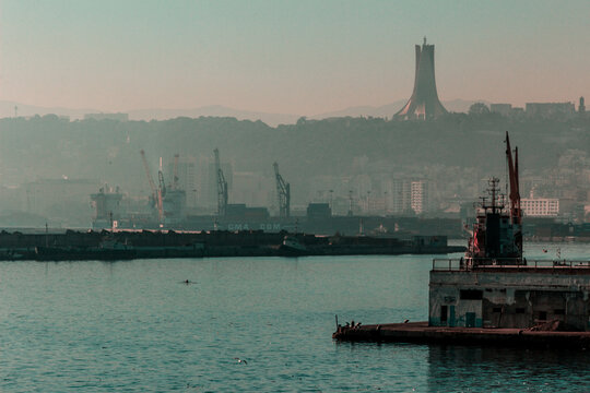 View of the Maqam Echahid monument overlooking the industrial port with cargo ships and cranes in Algiers, Algeria.