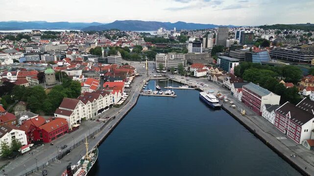 Aerial view of the historic Stavanger harbor with traditional white wooden buildings, boats docked at the pier, and the surrounding urban landscape in Stavanger, Rogaland, Norway.