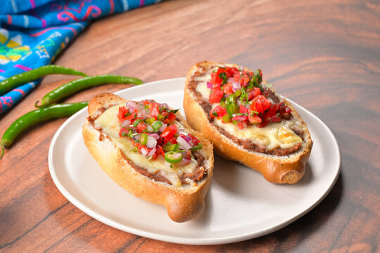 Traditional Mexican molletes topped with melted cheese, refried beans, and fresh pico de gallo on a white plate