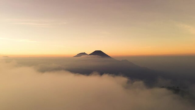 Aerial view of Gunung Prau rising above a thick sea of clouds during a golden sunrise in Wonosobo, Jawa Tengah, Indonesia.