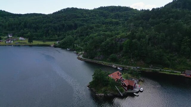 Aerial view of Sogne featuring traditional red wooden houses on a small island surrounded by calm water and lush green hills in Kristiansand, Agder, Norway.