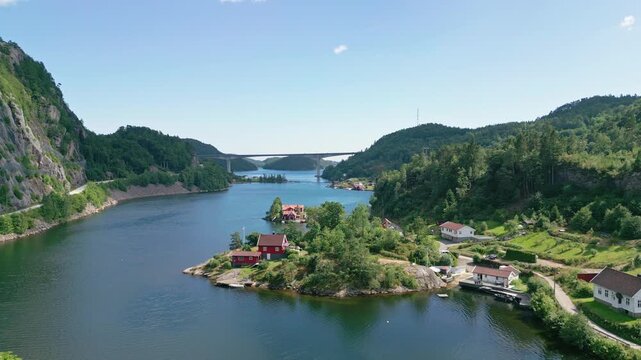 Aerial view of Sogne fjord featuring traditional red wooden houses on small islands surrounded by lush green hills and calm blue water in Kristiansand, Agder, Norway.