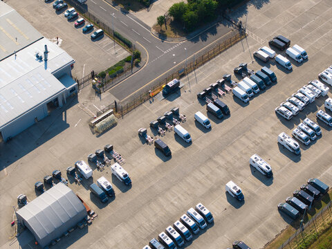 Aerial view of a large storage yard filled with numerous white camper vans and commercial vehicles parked in rows next to a warehouse building in Grimsby, England, United Kingdom.