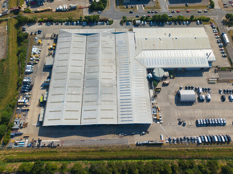 Aerial view of a large industrial warehouse facility with a corrugated metal roof, surrounding parking areas, and rows of parked vehicles in Grimsby, England, United Kingdom.