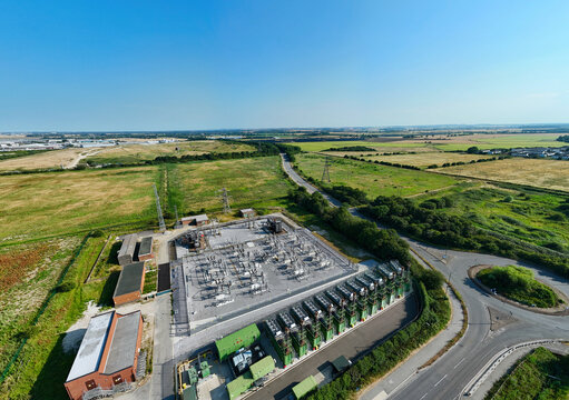 Aerial view of an electrical substation and containerized industrial generator compressor units situated in a rural landscape near a road in Immingham, England, United Kingdom.