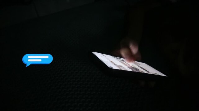 Person using a smartphone in the dark with a chat bubble icon.