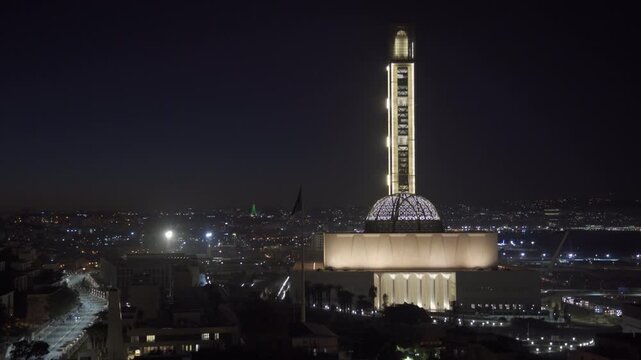 Aerial view of the illuminated Great Mosque of Algiers at night, showcasing its towering minaret and dome against the backdrop of the city lights in Algeria.