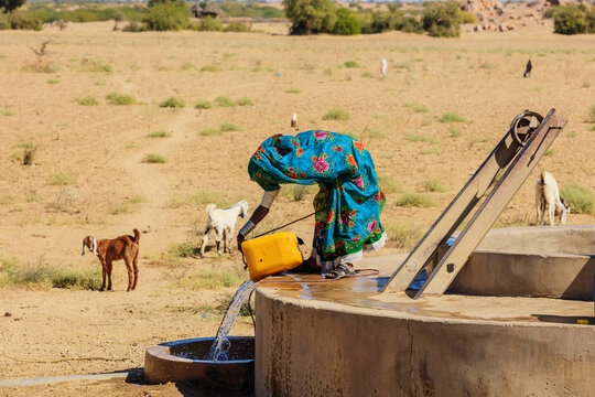 View of a woman in a vibrant traditional dress fetching water from a concrete well for her goats in the arid landscape of Nagarparkar, Sindh, Pakistan.