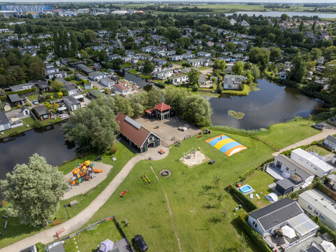Aerial view of De Holle Poarte holiday park featuring a playground, a jumping pillow, small canals, and numerous holiday homes nestled in green surroundings in Makkum, Friesland, Netherlands.