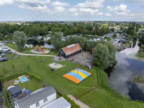 Aerial view of De Holle Poarte holiday park featuring a large colorful jumping pillow, playground equipment, and surrounding canals with mobile homes in Makkum, Friesland, Netherlands.