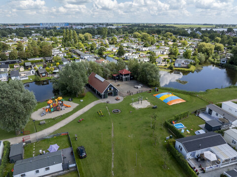 Aerial view of De Holle Poarte recreation park featuring a playground, a jumping pillow, and mobile homes situated near a pond in Makkum, Friesland, Netherlands.