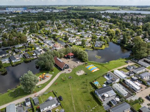 Aerial view of De Holle Poarte holiday park featuring numerous mobile homes, winding canals, a playground, and a jumping pillow in Makkum, Friesland, Netherlands.