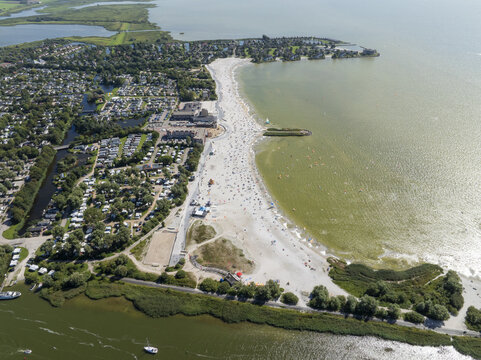 Aerial view of De Holle Poarte beach with holiday resort facilities, sandy shoreline, and people enjoying the water in Makkum, Friesland, Netherlands.