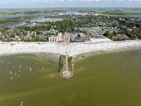 Aerial view of De Holle Poarte beach resort, featuring a sandy beach, a pier, holiday homes, and people enjoying the sunny weather in Makkum, Friesland, Netherlands.