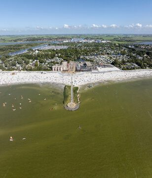 Aerial view of De Holle Poarte beach with people enjoying the sandy shore, a pier extending into the water, and surrounding greenery in Makkum, Friesland, Netherlands.