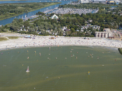 Aerial view of De Holle Poarte beach in Makkum with windsurfers on the water, a busy marina, and lush green surroundings in Makkum, Friesland, Netherlands.