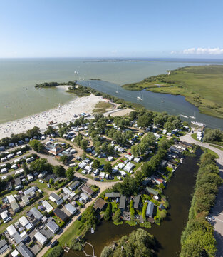 Aerial view of De Holle Poarte holiday park featuring a sandy beach, numerous caravans, and lush greenery situated along the IJsselmeer coast in Makkum, Friesland, Netherlands.