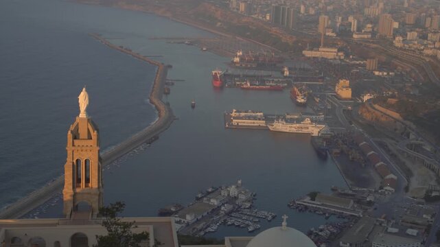 Aerial view of the historic Santa Cruz Chapel overlooking the bustling harbor and industrial port area with ships and boats in Oran, Oran Province, Algeria.