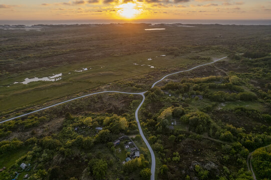 Aerial view of a winding bicycle path through the dunes and lush greenery at sunset in Terschelling, Friesland, Netherlands.