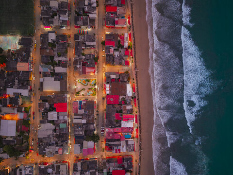 Aerial view of Montanita beach at dusk with illuminated buildings, streets, and ocean waves crashing on the shore in Montanita, Santa Elena, Ecuador.